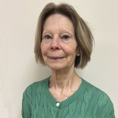 Leende kvinna i 60-årsåldern med gråbrun page, grön kofta.