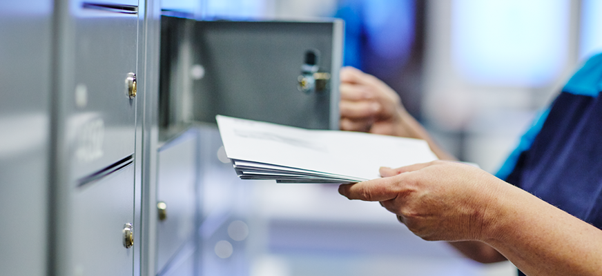 Närbild på en person som delar ut brev i en grå postbox.