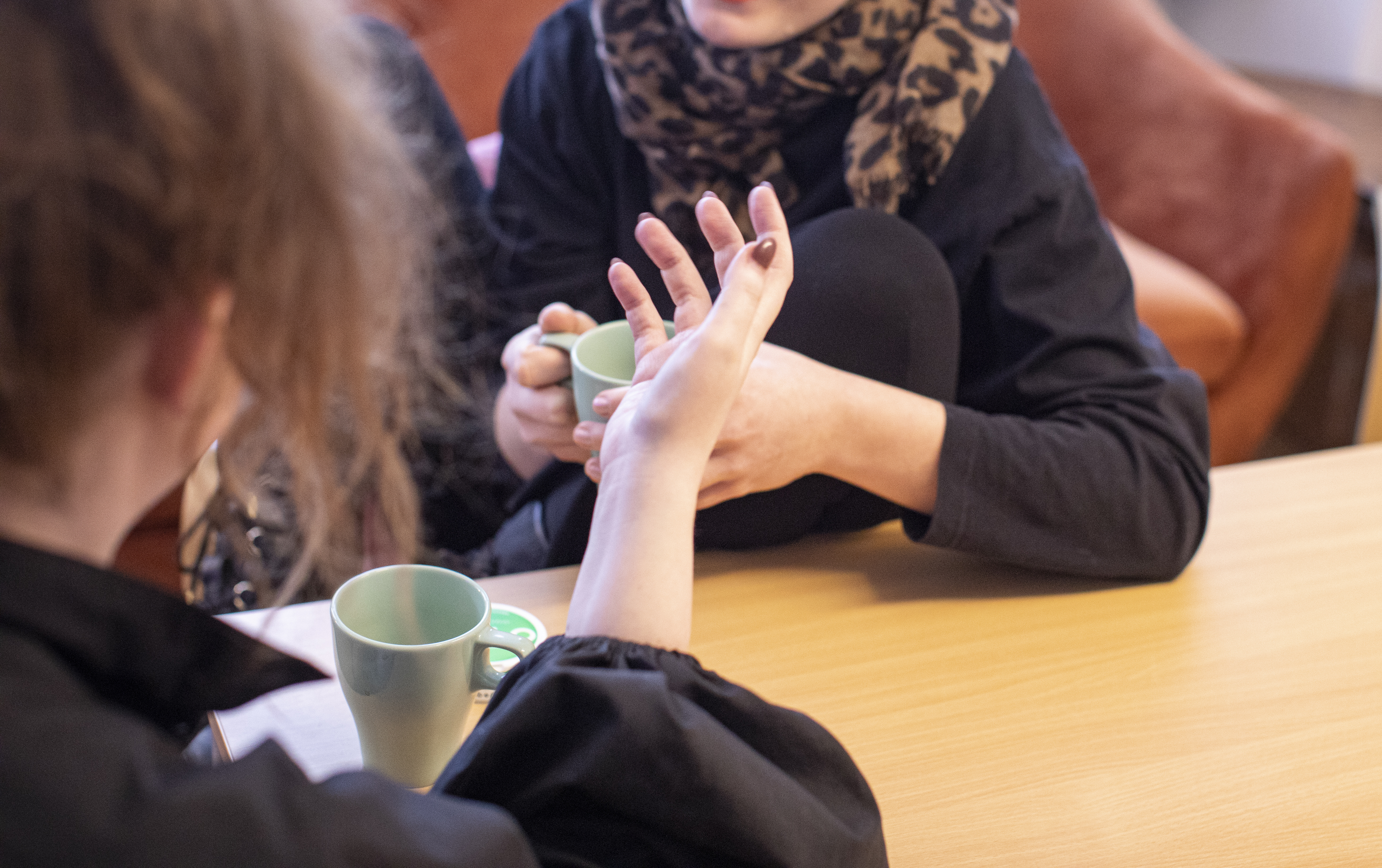 Två personer sitter mittemot varandra vid ett bord och pratar engagerat över en kopp kaffe.