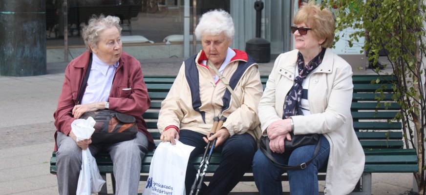 Tre äldre kvinnor sitter på en bänk och pratar