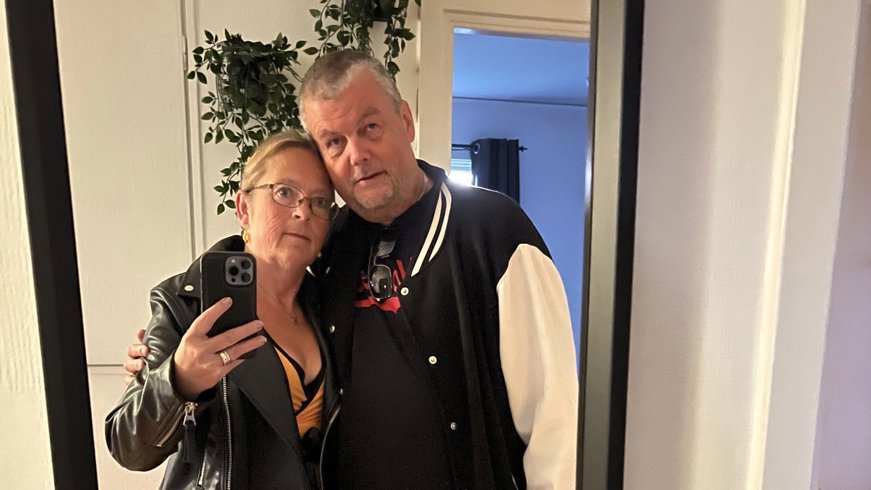 Ett par tar en spegelselfie inomhus. De står tätt intill varandra med armarna om varandra och tittar mot mobiltelefonen.