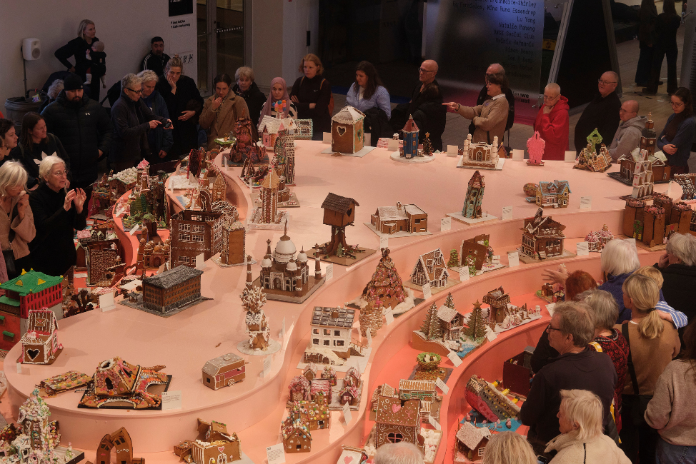 Från avstånd ser man ett svängt rosa podium i tre etager fylld med pepparkakshus i fantasifulla former. Runt podiet står människor och tittar och pekar.