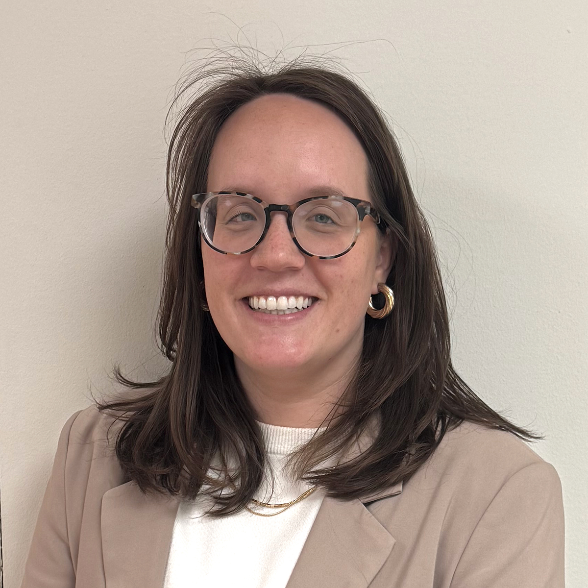 En leende kvinna i 30-årsåldern med brunt axellångt hår, beige kavaj och glasögon. 