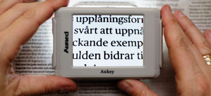 Ett par händer håller i ett förstoringsglas som visar förstorad text