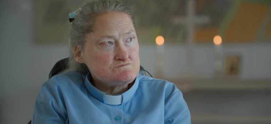 Maria E Norberg sitter i blå skjorta med prästkrage i en kyrka.