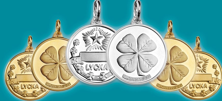 Berlocker med mönster som fyrklövrar och stjärnor, samt ordet "Lycka". Smyckena är i silver eller guld.