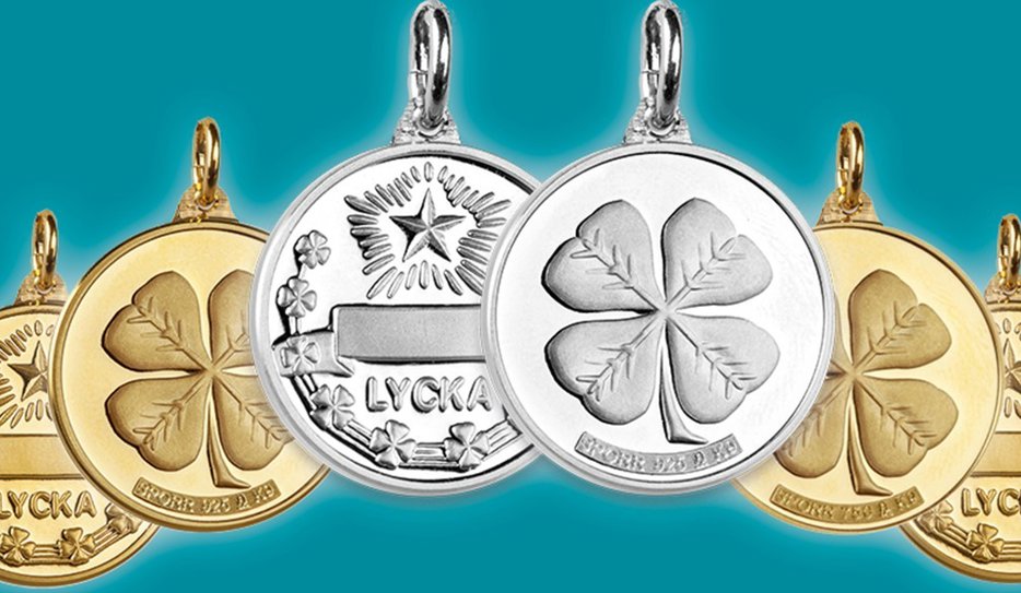 Berlocker med mönster som fyrklövrar och stjärnor, samt ordet "Lycka". Smyckena är i silver eller guld.