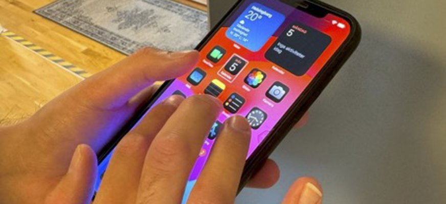 Händer som använder en smarttelefon, på skärmen syns olika app ikoner.