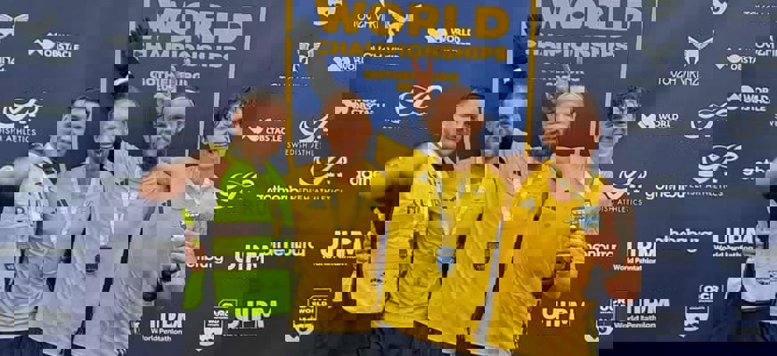 Tre gulklädda män och en manlig ledsagare i svarta kläder och gul väst poserar med medaljer framför en vägg med texten "OCR World Champions".