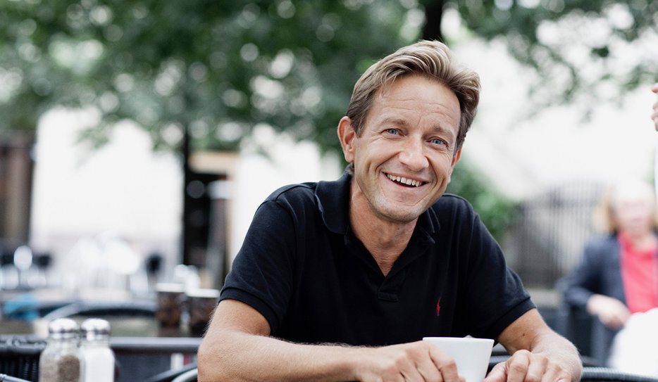 Porträttbild på Anders Kvanta som dricker kaffe och ler. Han har brunt hår och svart pikétröja.