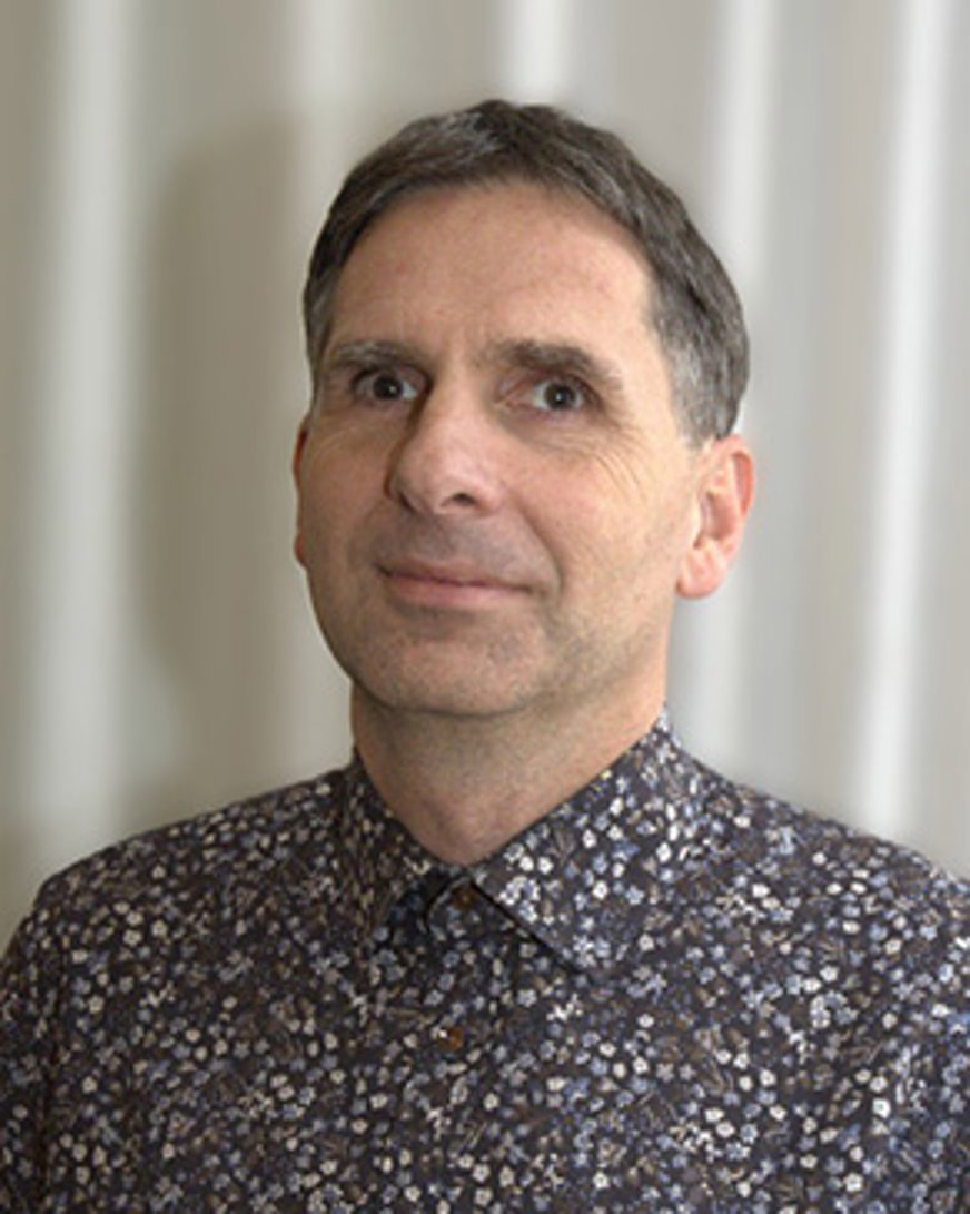 Porträttbild Karl Otto Rosenqvist: Medelålders man med mörkgrått hår klippt i kort frisyr. Han har en prickig skjorta i blått, grått och vitt,