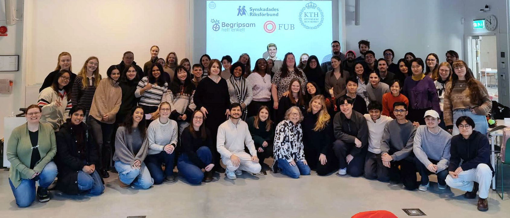Ett gruppfoto taget på slutet av ett diskussionsforum om tillgänglighet på KTH. Bilden visar cirka 50 studenter, både från Sverige men även från andra delar av världen, tillsammans med ansvarig lärare Sofia Strömqvist och rekryterade experter. Deltagarna står samlade i ett klassrum framför en projicerad display. På displayen i bakgrunden syns logotyper för KTH samt organisationerna Synskadades Riksförbund (SRF), FUB och Begripsam.