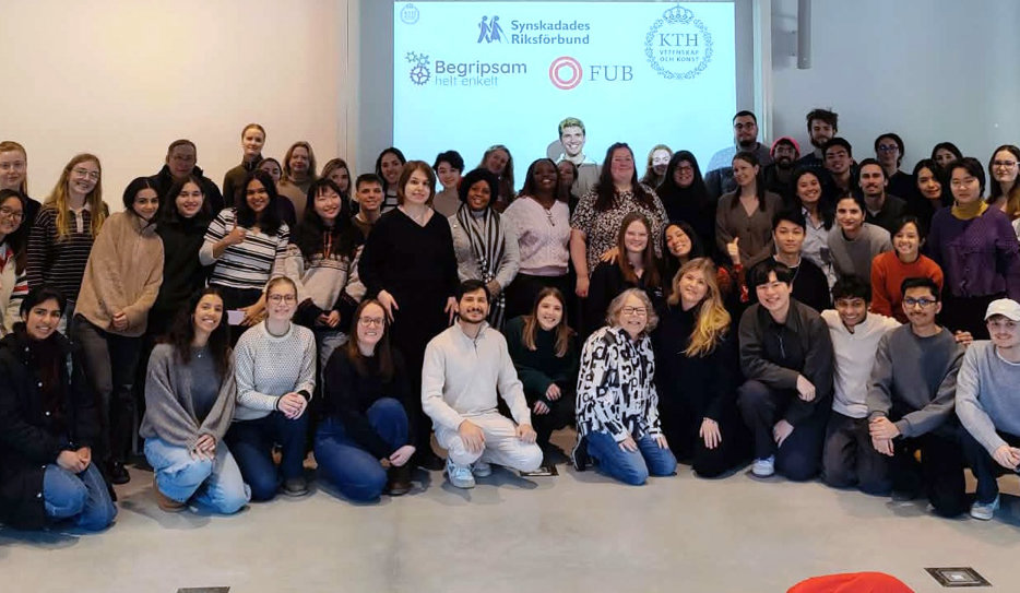 Ett gruppfoto taget på slutet av ett diskussionsforum om tillgänglighet på KTH. Bilden visar cirka 50 studenter, både från Sverige men även från andra delar av världen, tillsammans med ansvarig lärare Sofia Strömqvist och rekryterade experter. Deltagarna står samlade i ett klassrum framför en projicerad display. På displayen i bakgrunden syns logotyper för KTH samt organisationerna Synskadades Riksförbund (SRF), FUB och Begripsam.