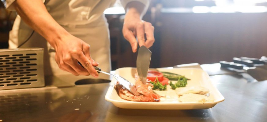 En kock fotad från midjan och nedåt lägger upp mat på en tallrik.