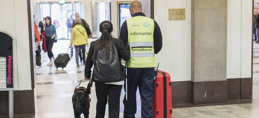 Kvinna med ledarhund ledsagas på station