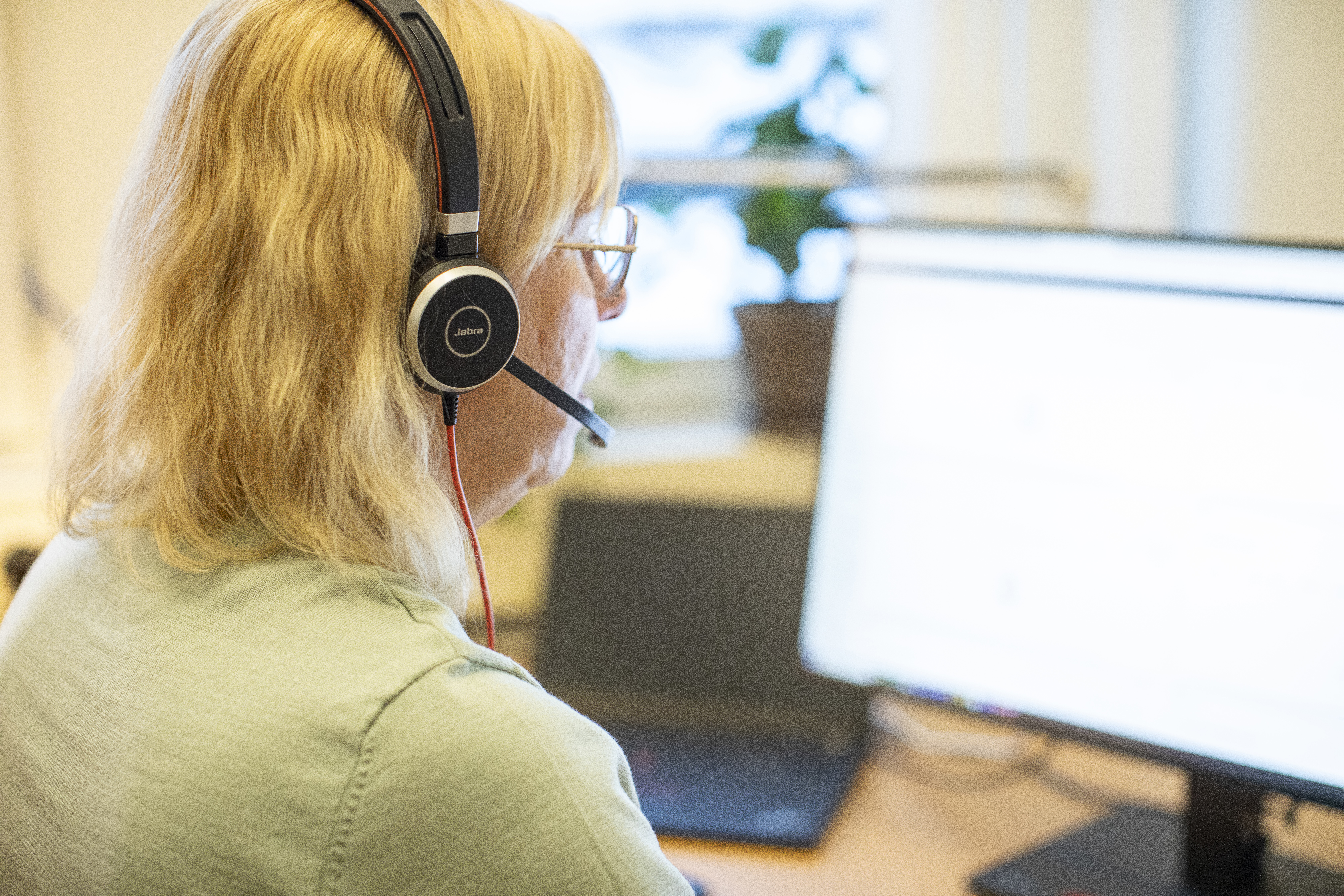 Kvinna sitter framför dator och pratar i telefon med headset.