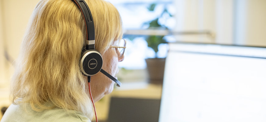 Kvinna sitter framför dator och pratar i telefon med headset.
