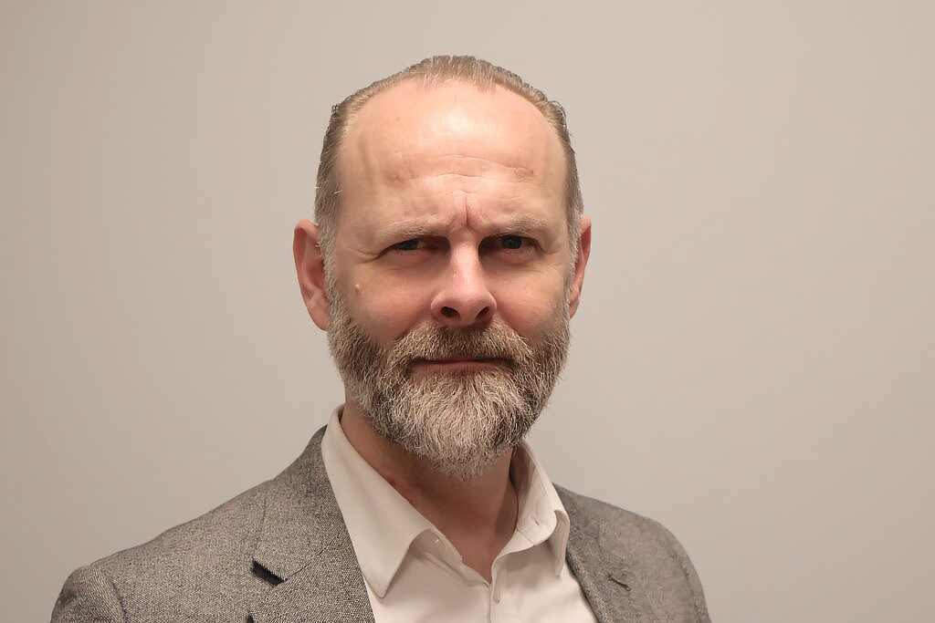 Klas Nelfelt, ordförande i Förbundet Sveriges Dövblinda, tittar in i kameran med allvarlig min. Han har grått skägg och bär kavaj med en ljus skjorta under. 