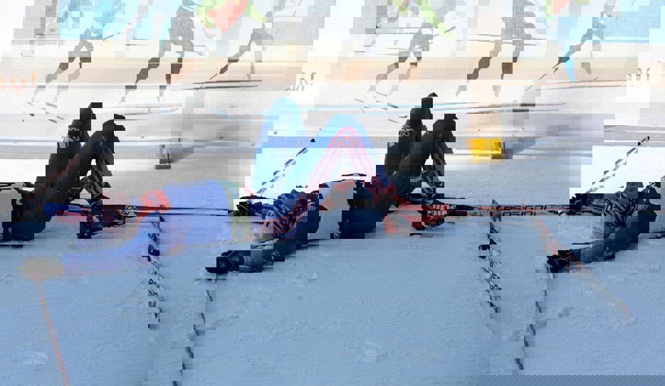 En längdskidåkare ligger på rygg efter avslutat lopp och andas ut.