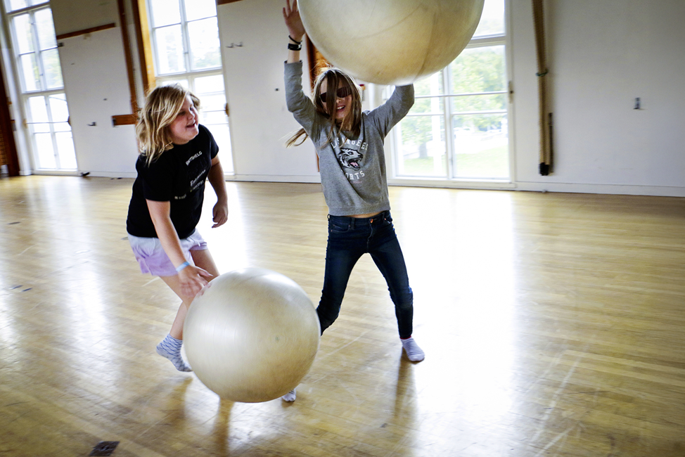 Två flickor leker med stora pilatesbollar i idrottssal.