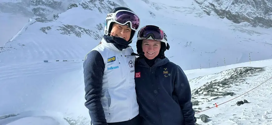 Alice Berntsson och guiden Regina Falk står alpint klädda i en skidbacke. Bakom dem syns ett snötäckt landskap.