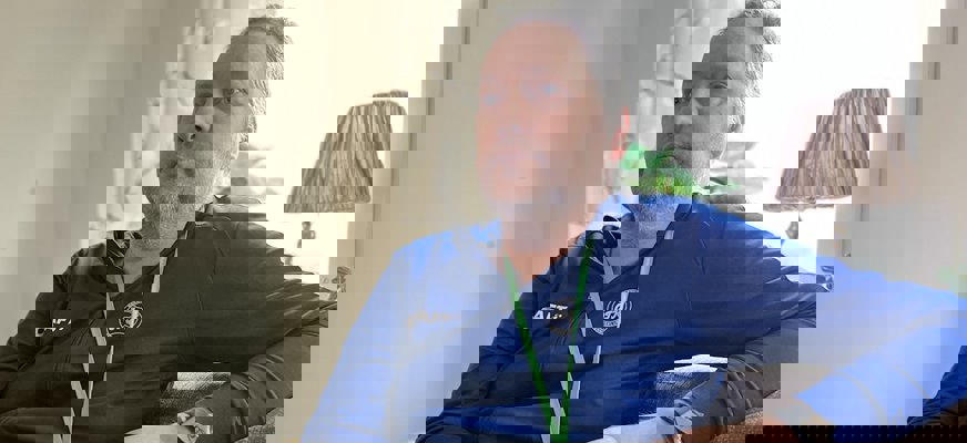 Johan Nyström sitter i en soffa framför ett fönster. Han har fingrarna flätade och lutar ena armen mot ryggstödet.