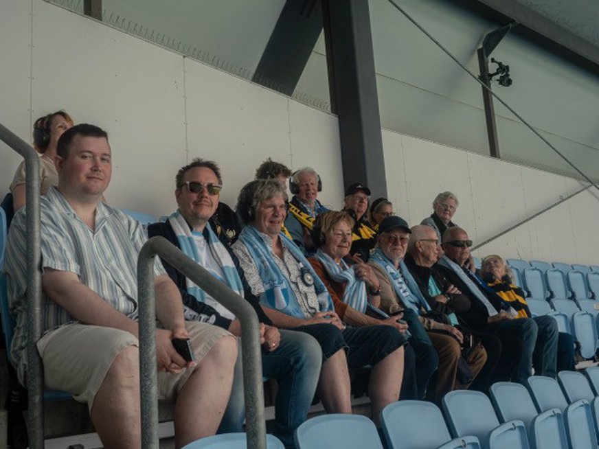 En gruppbild på de flesta av deltagarna när de sitter på två bänkrader och väntar på matchens början. Några med blåvita attribut och några med gulsvarta.