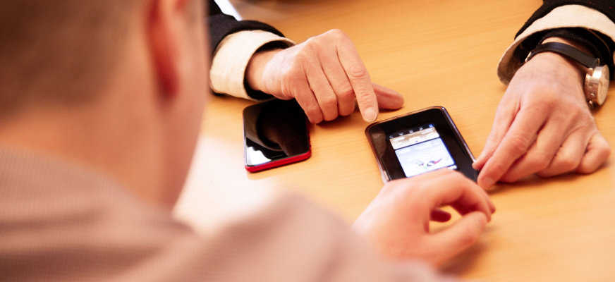 Yngre man hjälper äldre att använda sin mobiltelefon.