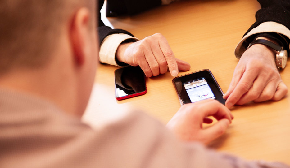 Yngre man hjälper äldre att använda sin mobiltelefon.