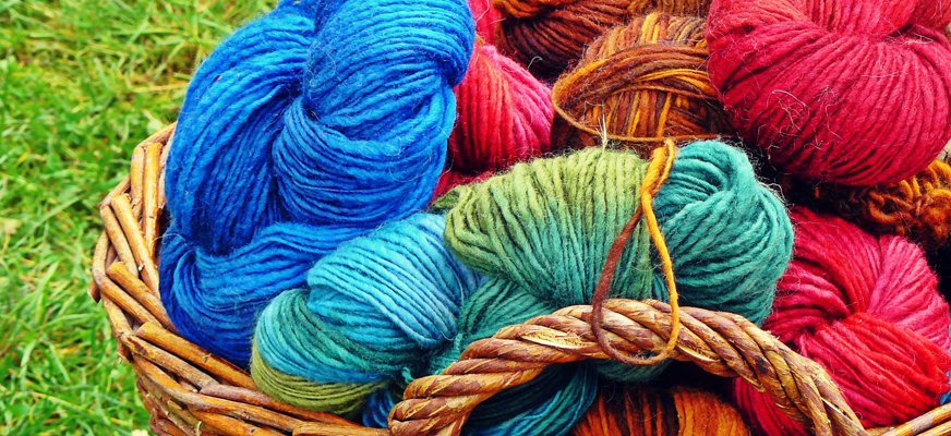 Bilden visar en flätad korg med massa färgglada garner i