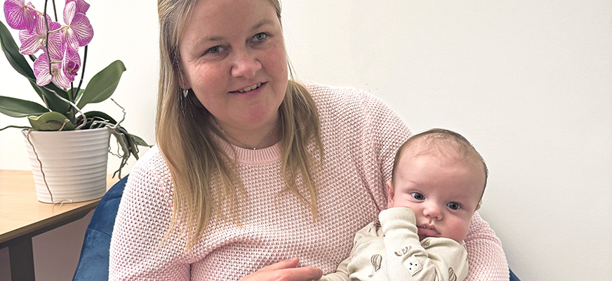 En blond kvinna med fräknar håller en liten bebis i famnen. Josefin ler och båda kollar mot kameran.