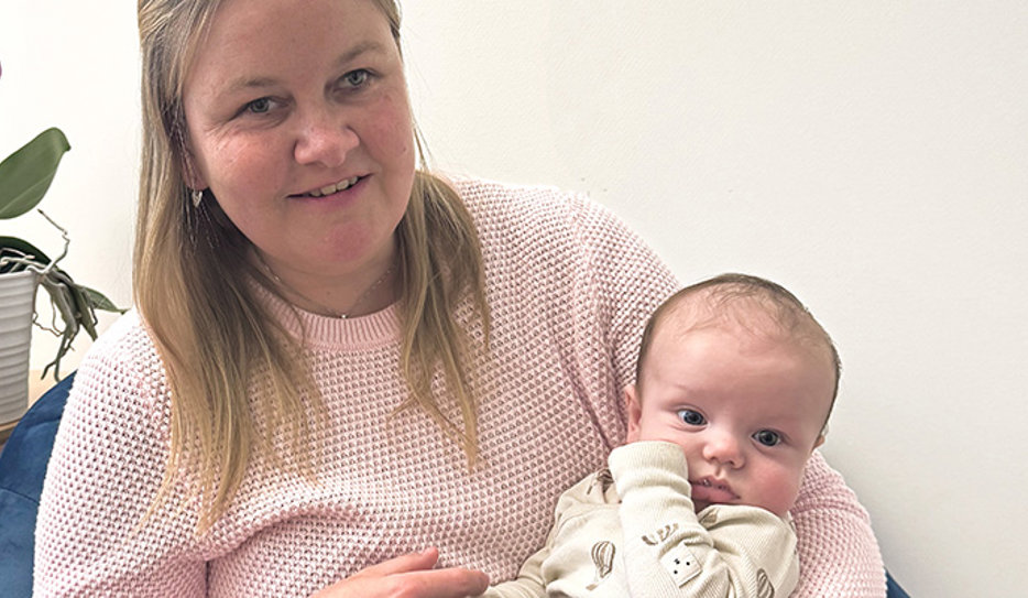 En blond kvinna med fräknar håller en liten bebis i famnen. Josefin ler och båda kollar mot kameran.