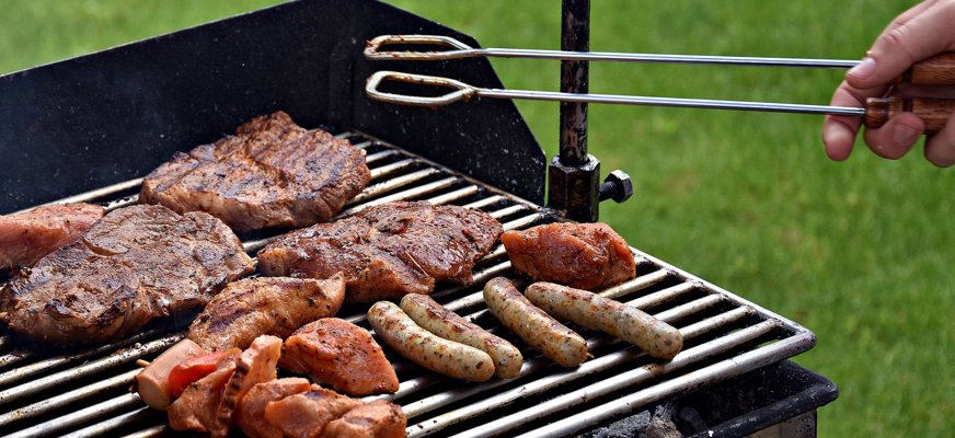 Bilden visar en grill med olika köttbitar och korvar på