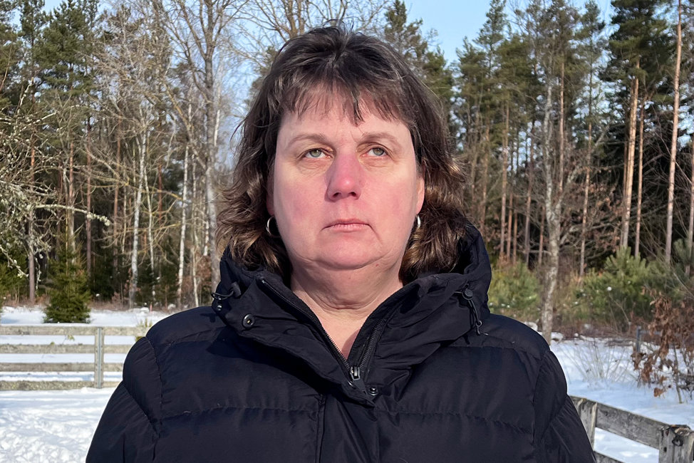 Mari är en medelålders kvinna i brunt, kortklippt hår med lugg. Hon har svart täckjacka och ringar i öronen. Mari står utomhus i en snöig hage och ser med bister min upp mot himlen.