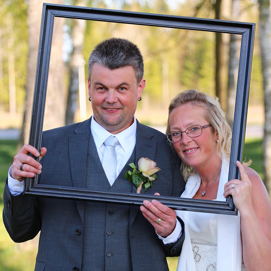 Ett brudpar som håller upp en tavelram framför sina ansikten, så det blir en "bild i bilden".