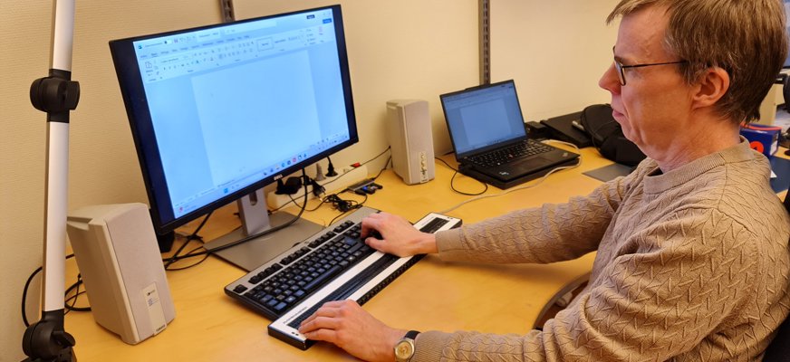 Patrik Johansson sitter vid sitt skrivbord. Han tittar på en datorskärm, har ena handen på ett tangentbord och andra handen på en punktdisplay.