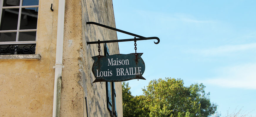 Fasaden på en gul gammal stenbyggnad med en skylt i gjutjärn. Skylten lyder "Maison Louis Braille".