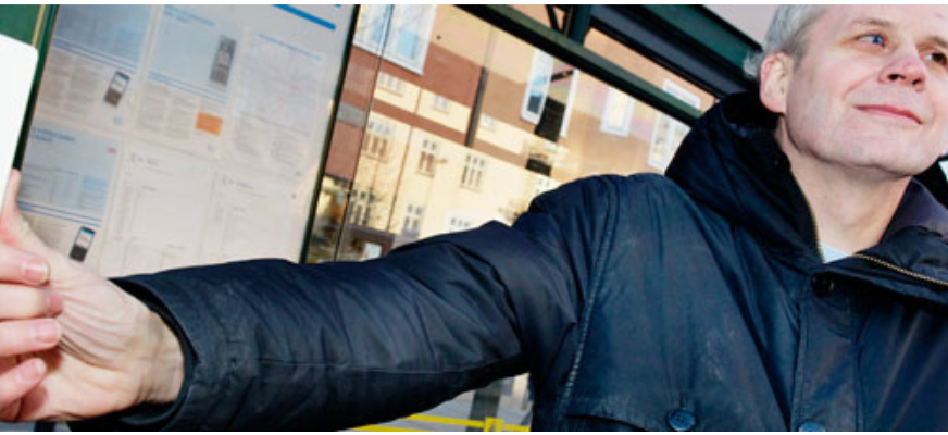 En man står i en busskur och trycker på en knapp till en talande elektronisk skylt