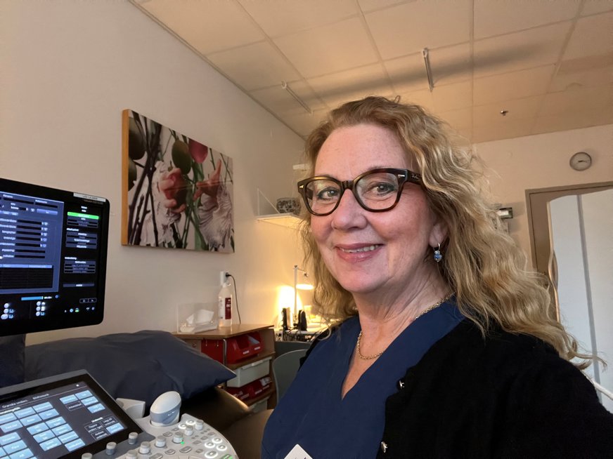 Nina Asplin i långt, lockigt, blont hår och blå skjorta. Hon har en namnskylt och glasögon.