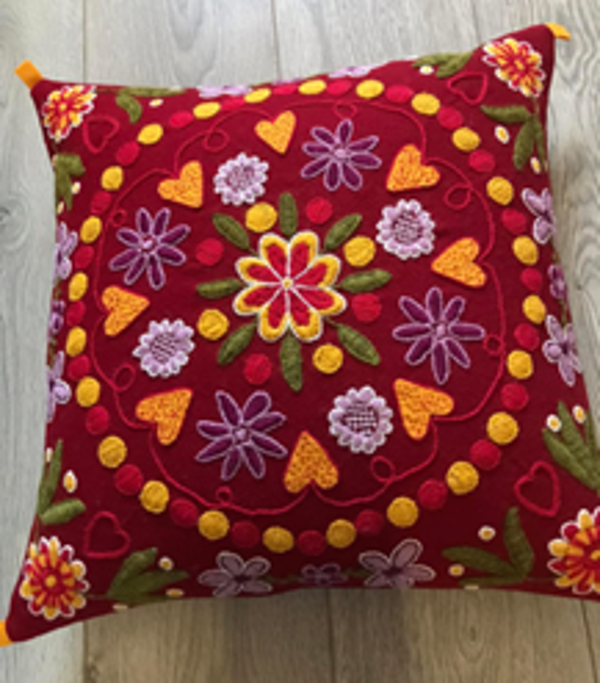 Röd kudde med diverse broderier i form av blommor, hjärtan med mera.