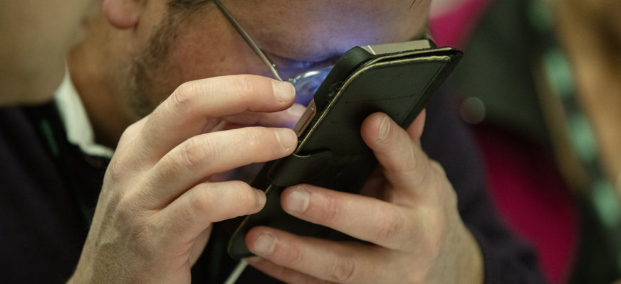 En mörkhårig man med glasögon tittar mycket nära på sin smartphone. 