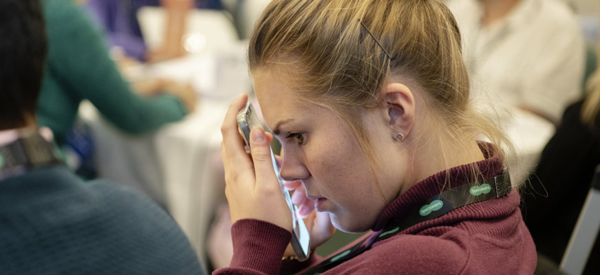 Kvinna med uppsatt hår försjunken i smartphone som hon håller tätt mot ansiktet