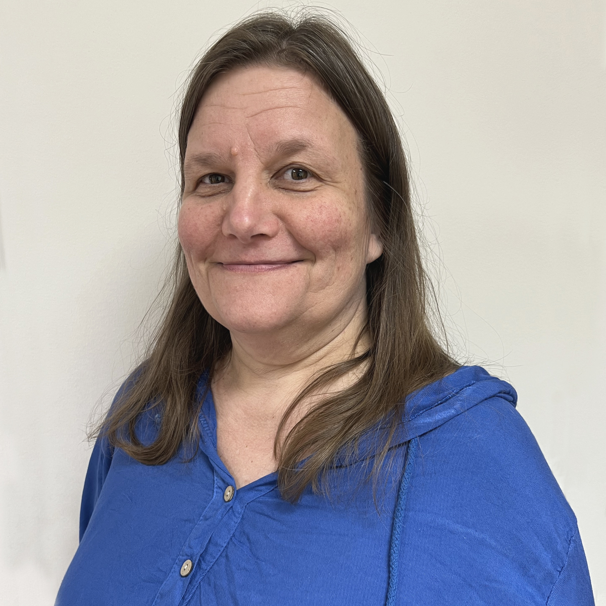 Leende kvinna i 50-årsåldern, brunt långt hår, klarblå tröja.