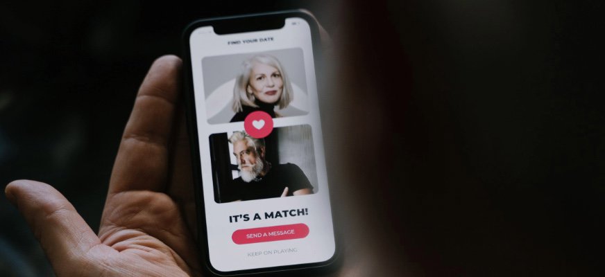 En hand håller en mobiltelefon som visar en dejtingapp. På skärmen syns två profilbilder och texten ”It’s a match!”.