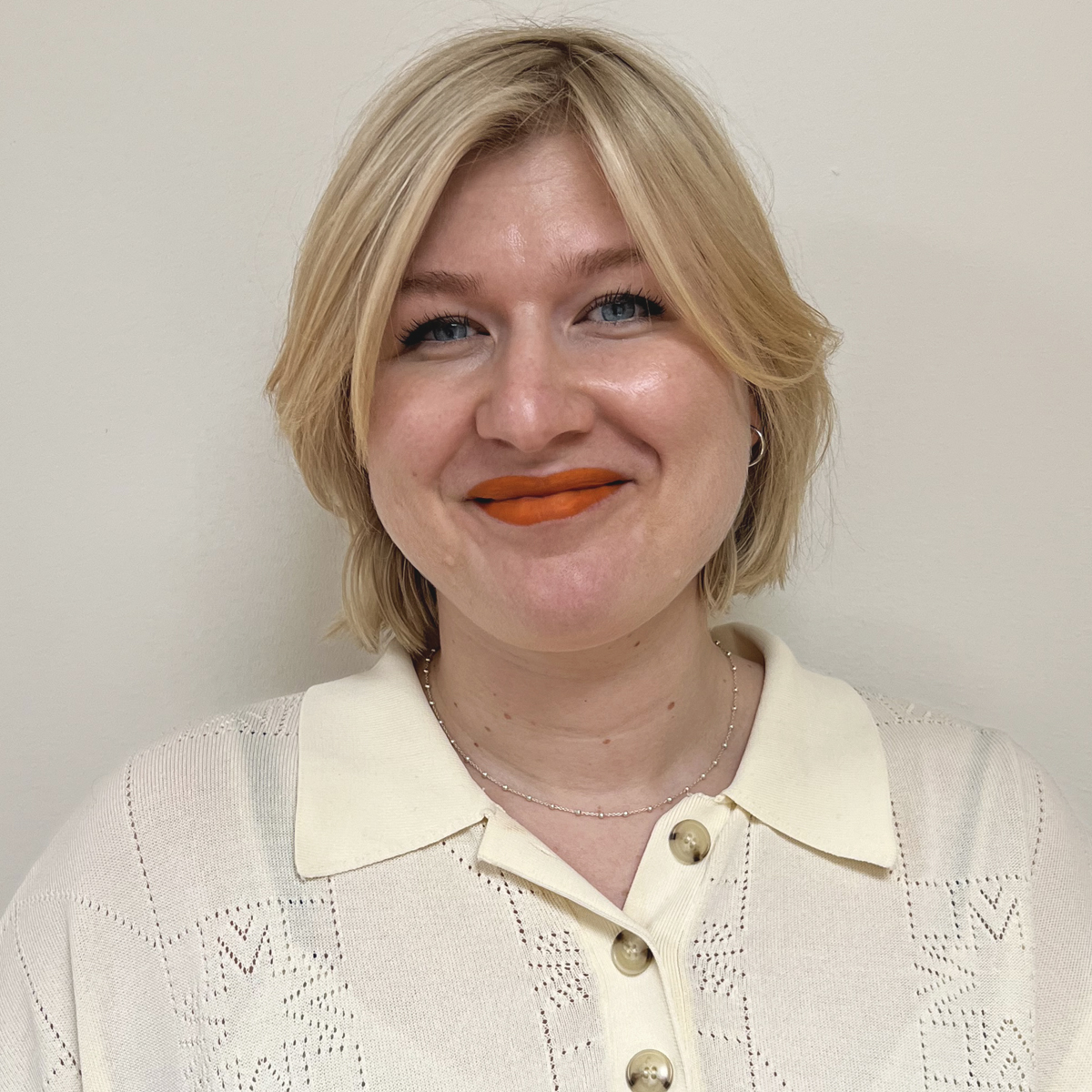 Ljus kvinna 30-årsåldern, blond page, orange läppstift, vit skjorta.