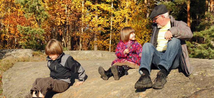 Två barn och en äldre man sitter på ett berg