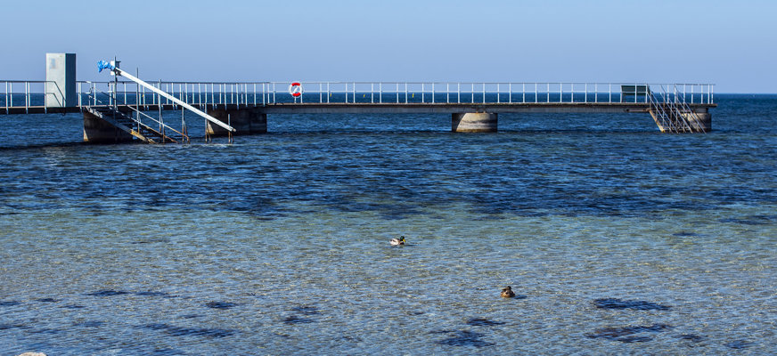 Bilden visar den långa bryggan vid Öresunds Funkis. Räckena är vita och det finns trappor ner i havet och en frälsarkrans.