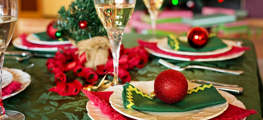 Bilden visar en julbordsdukning med grön duk, glas med bubbel, julgran i bakgrunden och julgranskulor på tallrikarna