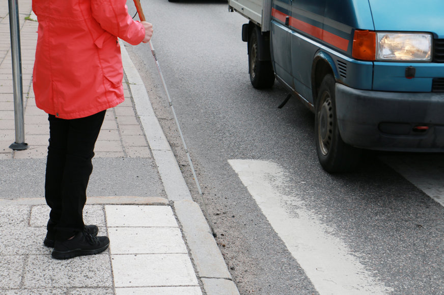 Person med käpp väntar vid övergångsställe