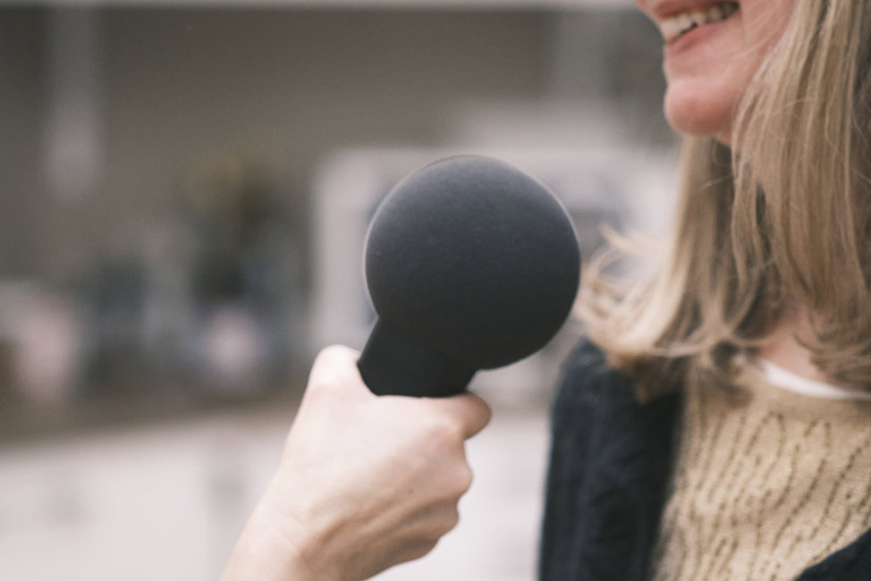 En kvinna i bakgrunden pratar in i en mikrofon. Foto: Gemini AI